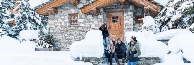 Gruppo di amici che ride davanti a uno chalet innevato in Val d'Isère in inverno