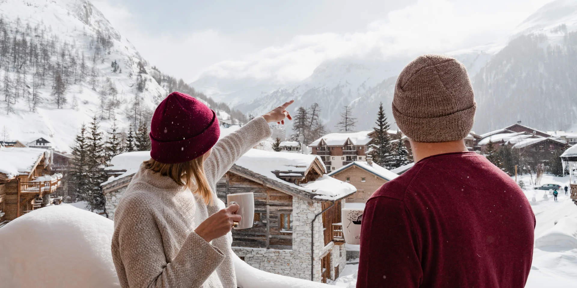 Due persone (amici o coppia) sul balcone innevato di uno chalet in Val d'Isère in inverno